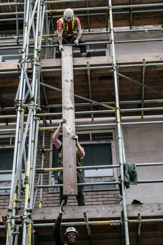 Workers lifting scaffold boards during setup on a renovation project