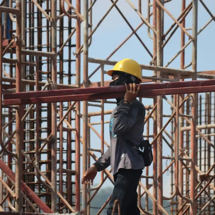 Construction worker carrying scaffold beams at a busy project site in San Rafael