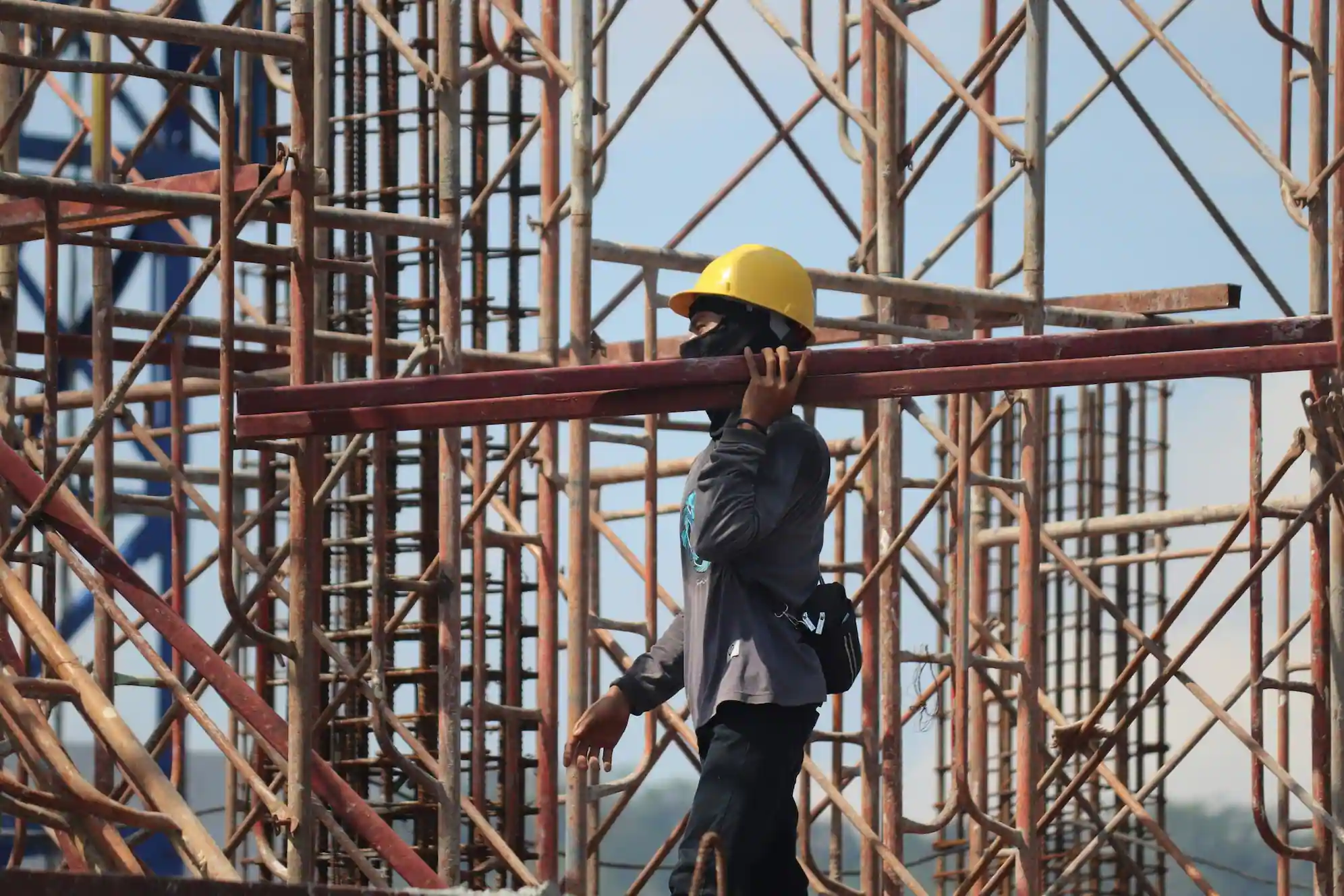 Construction worker carrying scaffold beams at a busy project site in San Rafael